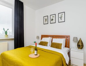 A hotel room with a bed, a bedside table, a lamp, and a window with a curtain. - Spacious Central Warsaw Apartment (Warsaw)