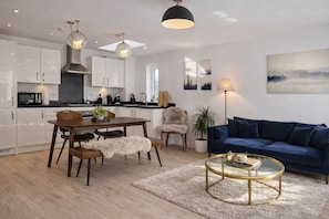 Eine moderne Küche mit weißen Schränken, einem Esstisch mit Stühlen und einem blauen Sofa im Wohnbereich.