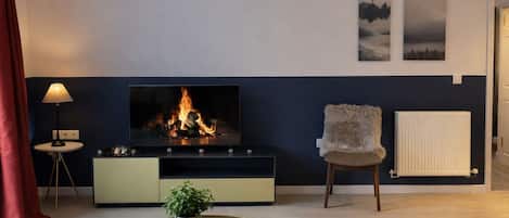 A modern living room with a flat-screen TV, a fireplace, a sofa, a chair, and a small table with a plant.
