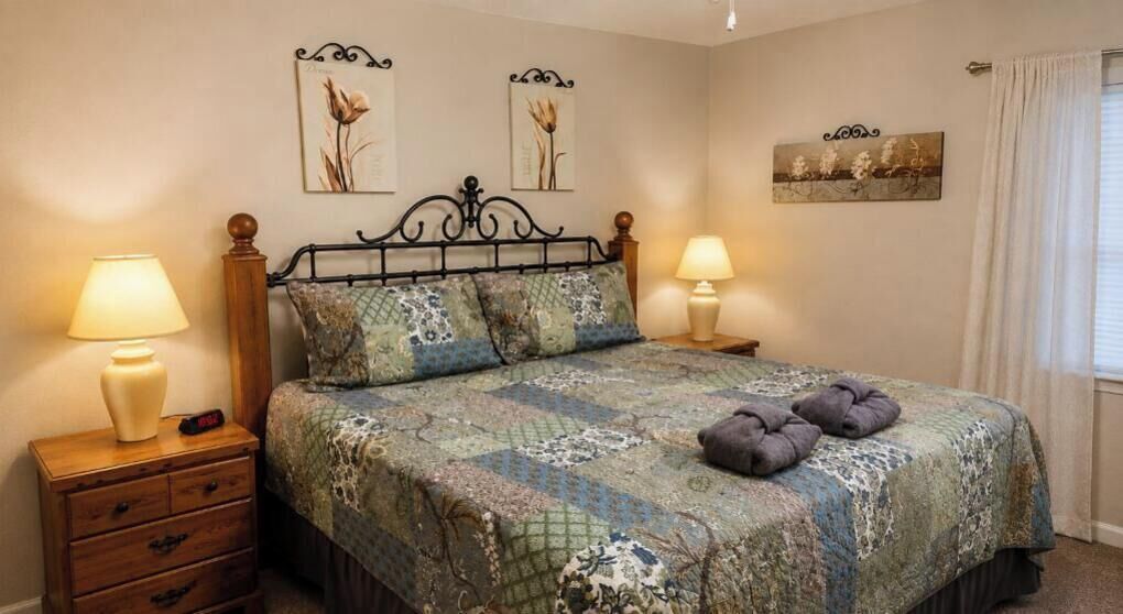 Une chambre à coucher avec un lit, deux tables de chevet, des lampes et des œuvres d’art accrochées aux murs.