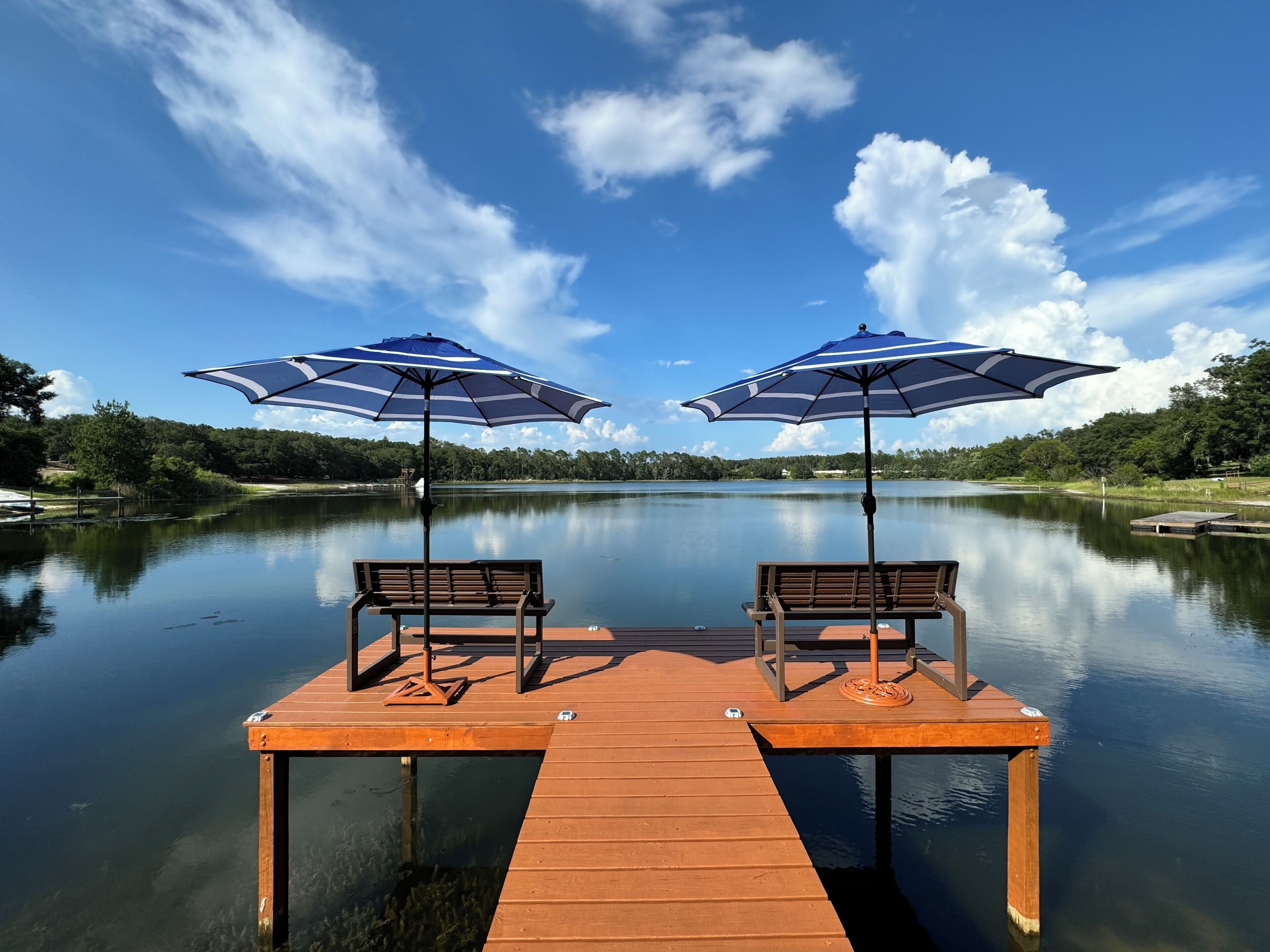 A wooden dock with two benches and two blue umbrellas.