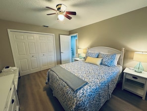 A bedroom with a bed, two nightstands, a ceiling fan, and a door.