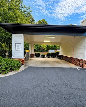 A covered parking area with a brick wall and a signboard. - Presidential 1BR Suite-Adjustable Bed & Seating-Resort Pool, Gym & Clubhouse (Charlotte)