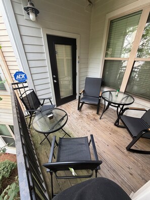Un espace extérieur abrité avec une table et des chaises en verre, une porte portant un panneau d’avertissement de sécurité et une fenêtre avec des stores.