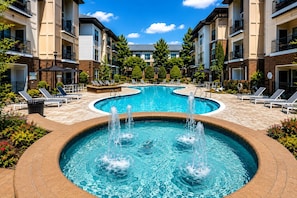 A swimming pool with a fountain, surrounded by lounge chairs and a brick walkway. - Presidential 1BR Suite-Adjustable Bed & Seating-Resort Pool, Gym & Clubhouse (Charlotte)