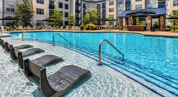 A swimming pool with clear water, lounge chairs, and a brick patio area.