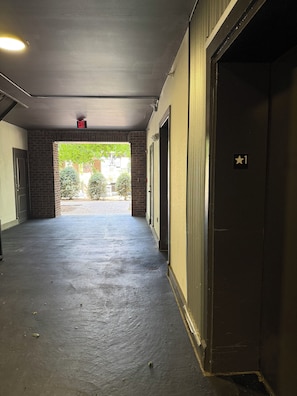 A corridor with a concrete floor, a brick wall, and a door marked with a star symbol. - Presidential 1BR Suite-Adjustable Bed & Seating-Resort Pool, Gym & Clubhouse (Charlotte)