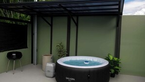 Un bain à remous installé sous une terrasse couverte avec une structure en métal, une poubelle et une petite table.