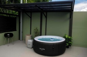 A hot tub under a covered patio with a metal frame, a trash can, and a small table. - Cozy 1-bedroom house La Fortuna with AC volcano view, swimming pool and Jacuzzi (La Fortuna)