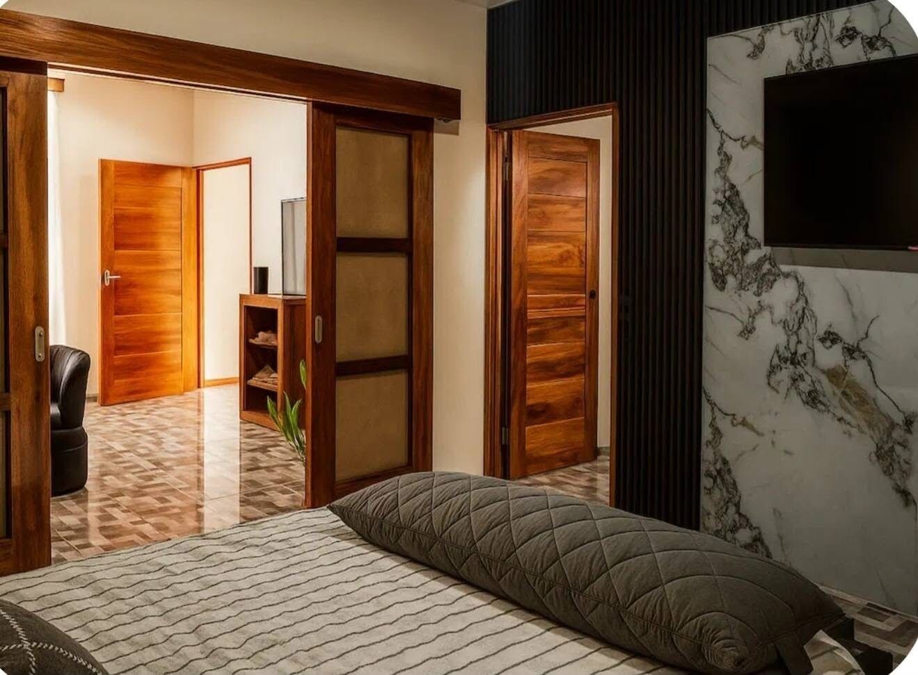 A bedroom with a bed, a TV mounted on the wall, and a wooden wardrobe.