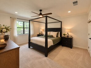 A four-poster bed with a ceiling fan, bedside tables with lamps, a vase with flowers, and a window with curtains. - 3-bedroom near Texas A&M Campus! (College Station)