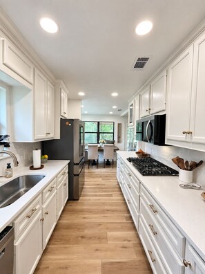 A kitchen with white cabinets, a stainless steel sink, and a central island with a stove. - 3-bedroom near Texas A&M Campus! (College Station)