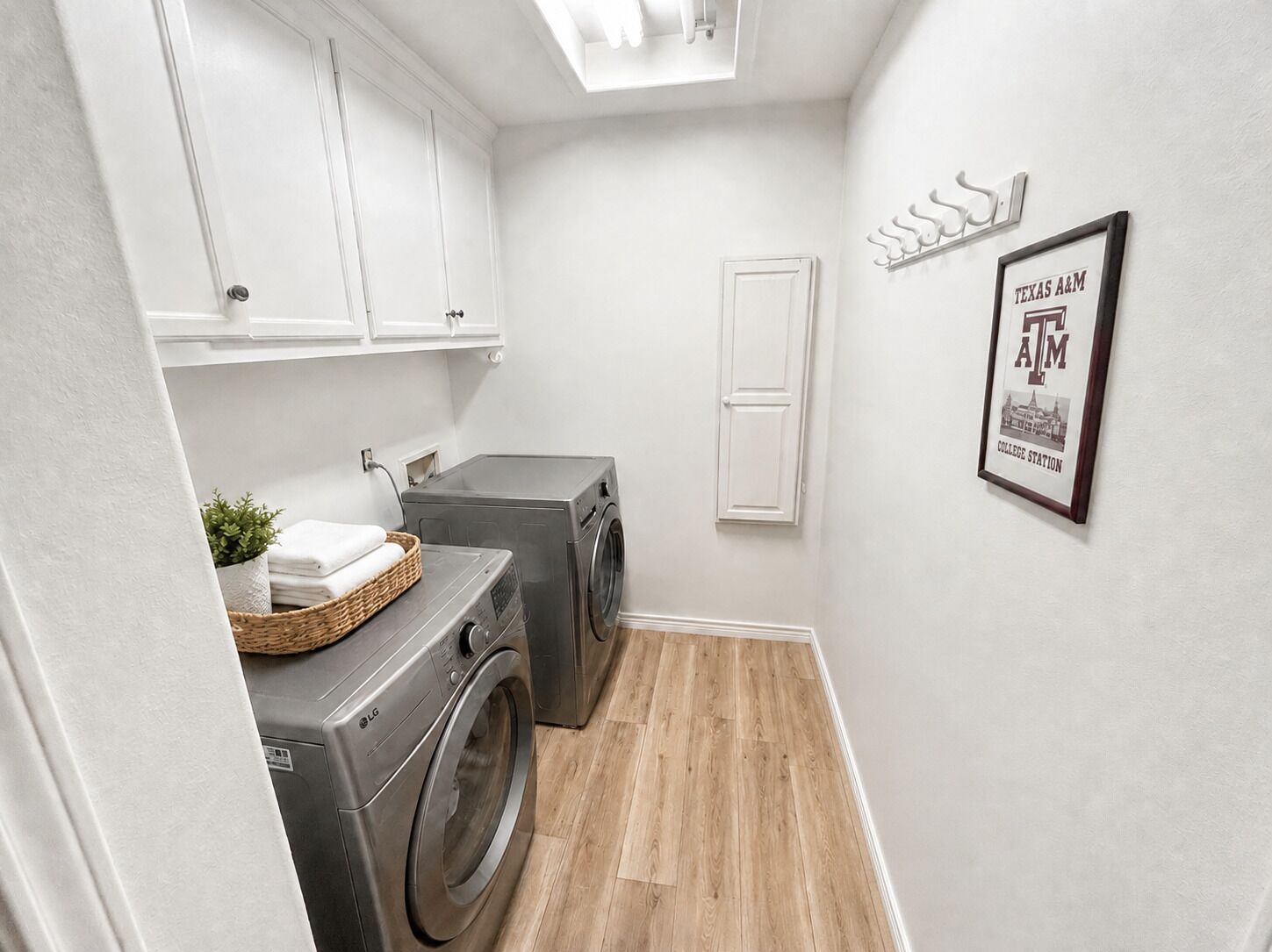 A laundry room with two front-loading washing machines, a basket with folded towels, and a framed picture on the wall.