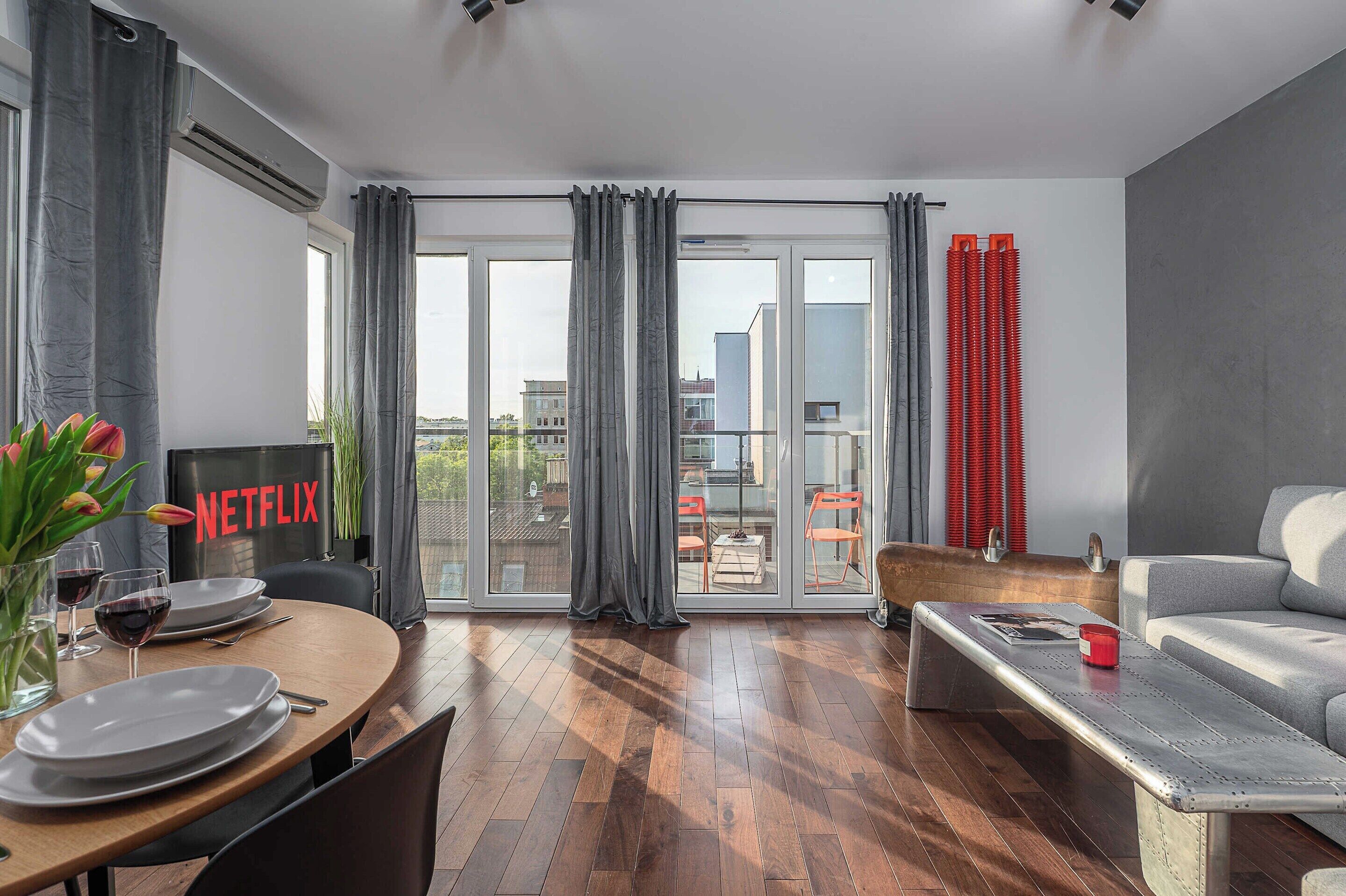 Un salon moderne comprenant un coin repas, un canapé, une table basse et un balcon agrémenté de rideaux rouges.