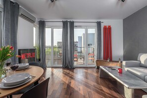 A modern living room with a dining area, a sofa, a coffee table, and a balcony with red curtains. - Warsaw Flat Near Praga Park (Warsaw)