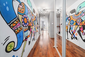 A hallway with colorful murals on the walls, wooden flooring, and a modern light fixture. - Warsaw Flat Near Praga Park (Warsaw)