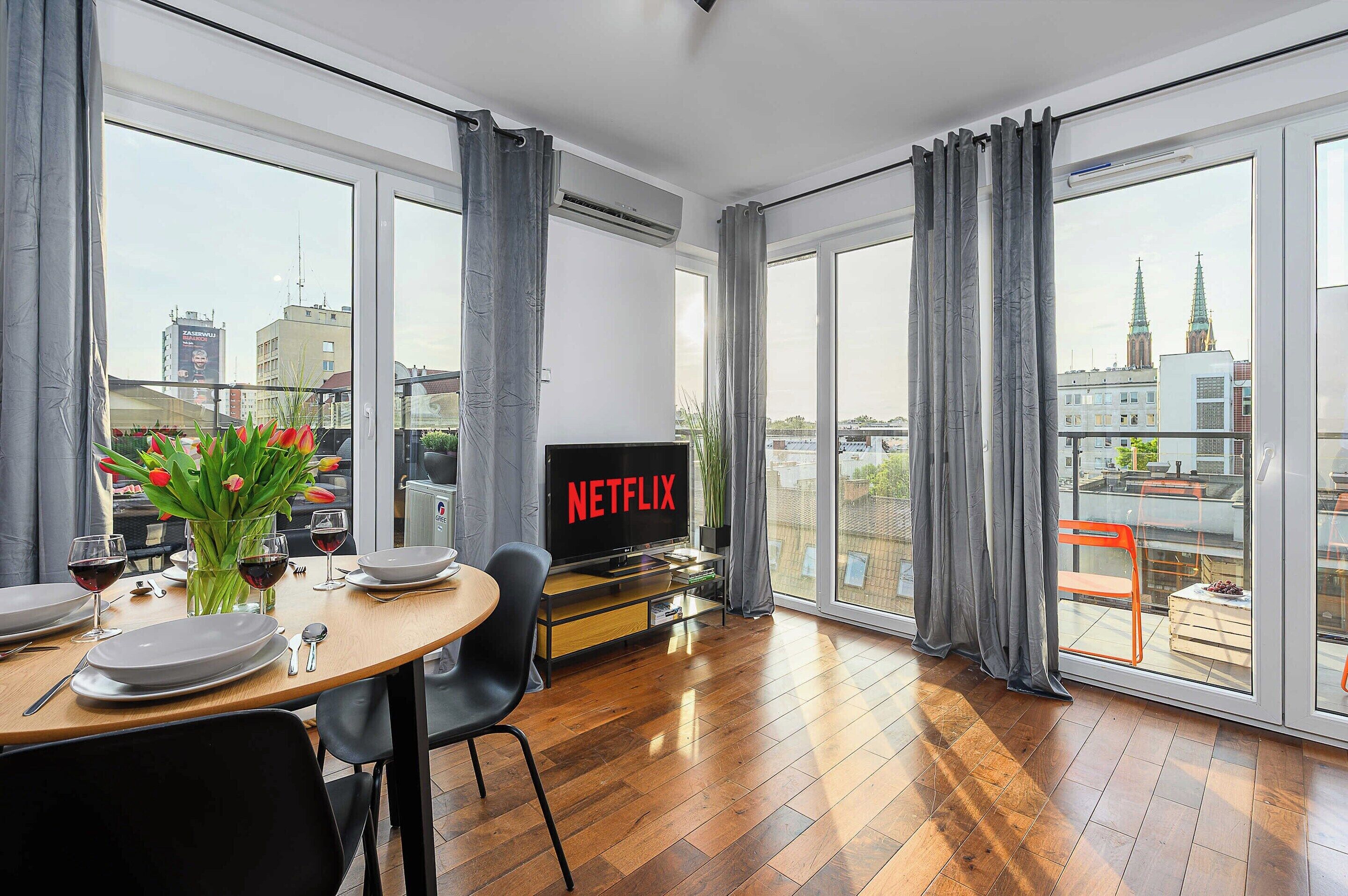 A modern living room with a dining area, large windows, and a view of the cityscape.