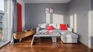 Ein modernes Wohnzimmer mit einem grauen Sofa, roten Kissen, einem Couchtisch und einem großen Fenster mit Vorhängen.