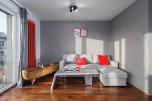 Ein modernes Wohnzimmer mit einem grauen Sofa, roten Kissen, einem Couchtisch und einem großen Fenster mit Vorhängen.