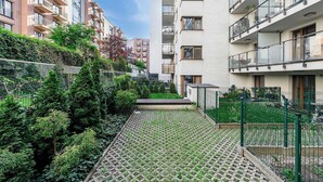Ein Wohngebäude mit mehreren Balkonen, einem gepflasterten Weg und einem Garten mit verschiedenen Pflanzen.