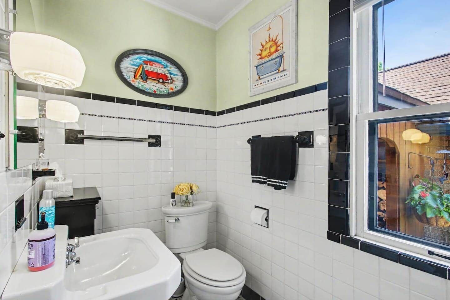 A bathroom with a toilet, sink, and a window with a view of plants.