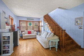 A living room with two striped sofas, a wooden staircase, and a bookshelf. - Unsalted Tides-Walk to Beach + Town + Dog-Friendly (South Haven)