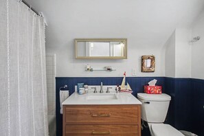 Ein Badezimmer mit weißem Waschbecken, einem Spiegel, einer Toilette und einer Duschvorhang.