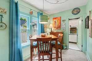 A dining area with a wooden table and chairs, a hanging light fixture, and a view through a window. - Unsalted Tides-Walk to Beach + Town + Dog-Friendly (South Haven)