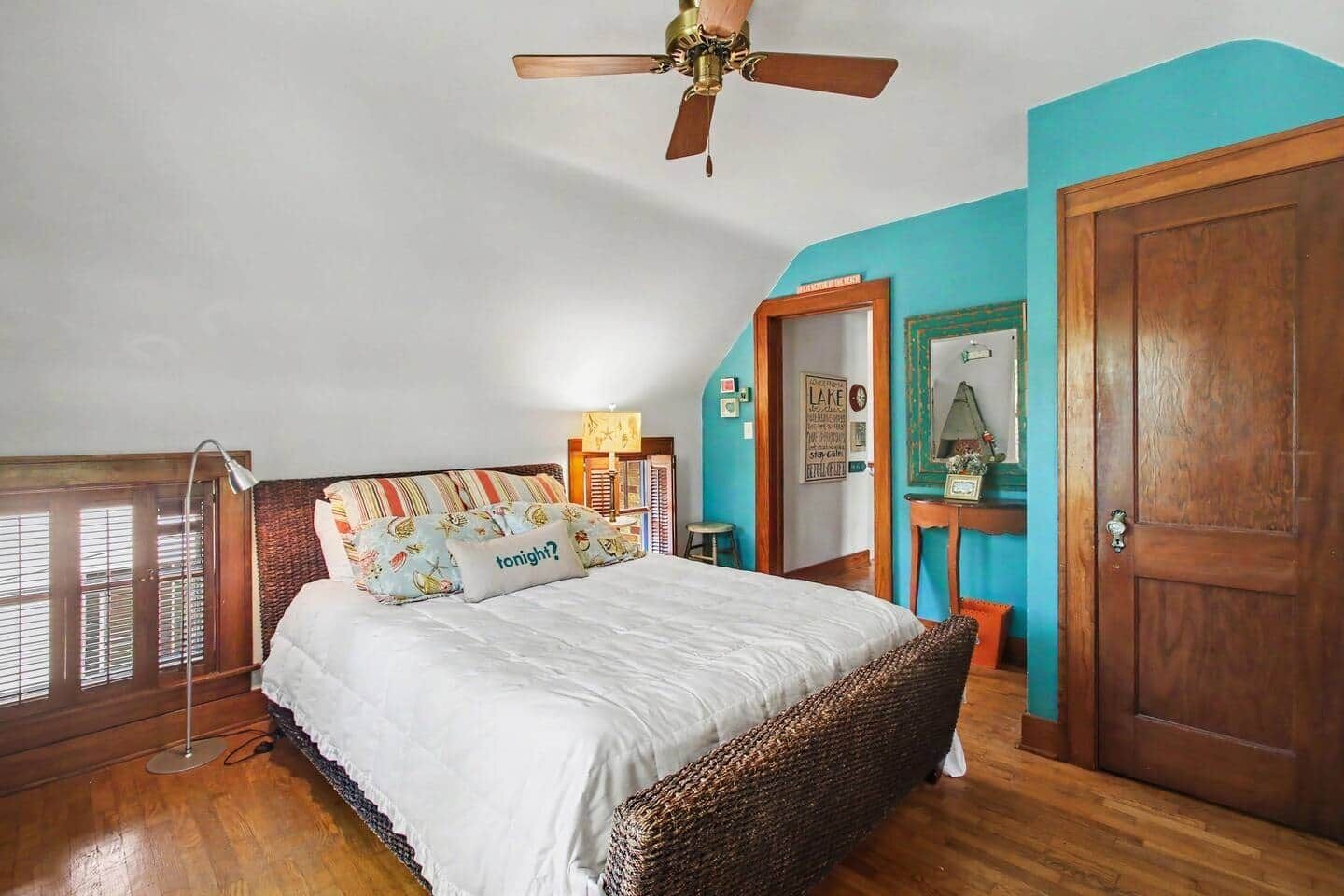A bedroom with a bed, a ceiling fan, a wooden door, and a window with blinds.