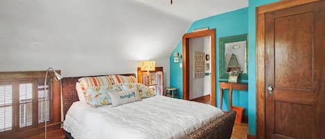 Ein Schlafzimmer mit Bett, Deckenventilator, Holztür und Fenster mit Jalousien.