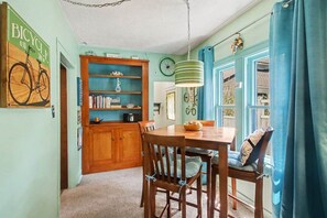 A dining area with a wooden table and chairs, a bookshelf, and a bicycle-themed wall decoration. - Unsalted Tides-Walk to Beach + Town + Dog-Friendly (South Haven)