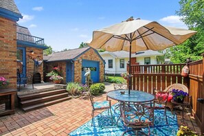 A patio with a round table and chairs, a large umbrella, and a brick pathway leading to a house. - Unsalted Tides-Walk to Beach + Town + Dog-Friendly (South Haven)