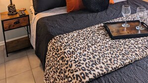 Quarto com cama, mesas de cabeceira, espelho e janela com cortinas.