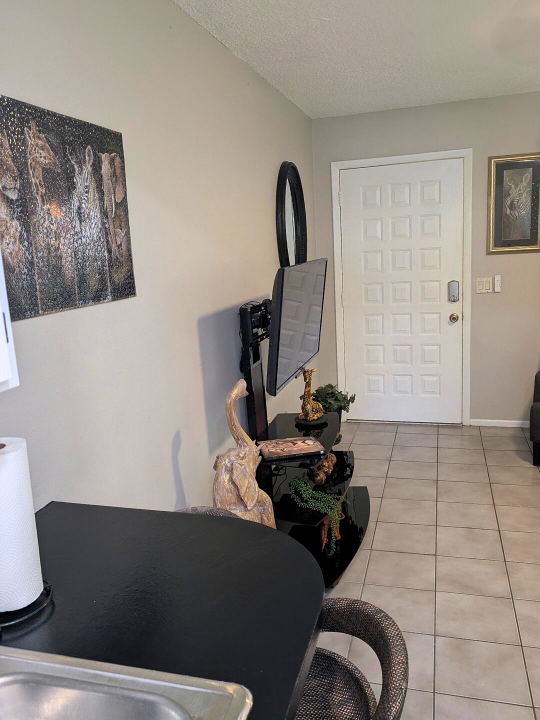 A room with a dining table, a mounted television, a door, and a framed picture on the wall.