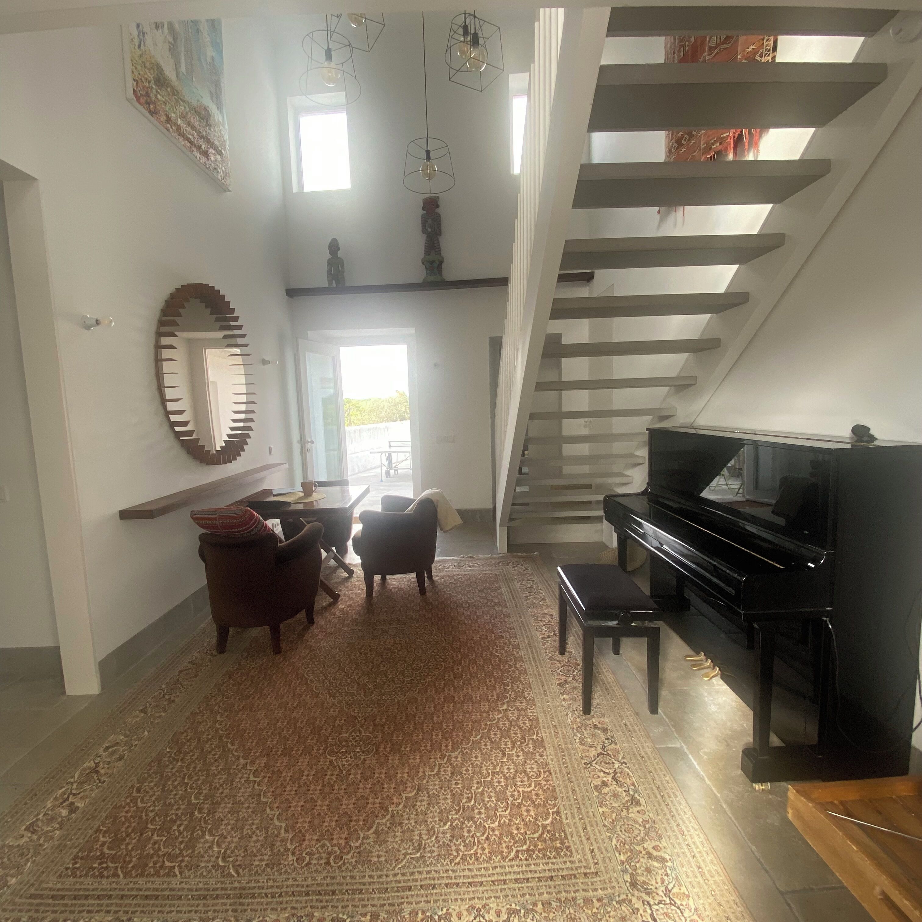 Una sala de estar con un piano, una escalera y un ventanal grande.