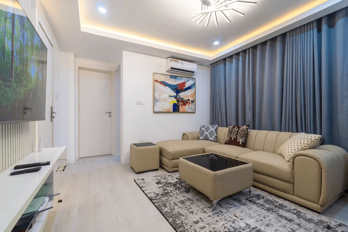 Una sala de estar moderna con un sofá, un reposapiés y un televisor de pantalla plana.