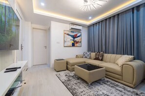 Una sala de estar moderna con un sofá, un reposapiés y un televisor de pantalla plana.