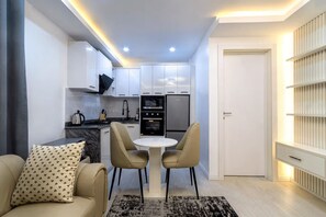 Cocina compacta con armarios blancos, horno negro y microondas. Cuenta con una zona de comedor con una mesa redonda y dos sillas.