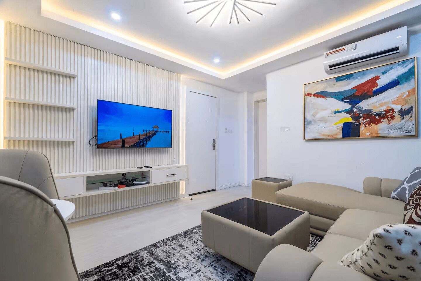 A modern living room with a flat-screen TV, a sofa, a coffee table, and a painting on the wall.