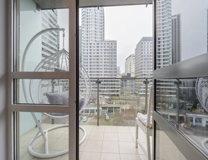 A balcony with a view of high-rise buildings, a hanging chair, and a white bench. - City Apartment With Balcony (Warsaw)
