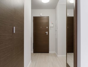 A hallway with a wooden door, a white wall, and a light switch. - City Apartment With Balcony (Warsaw)
