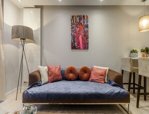 A modern living room with a sofa, a floor lamp, a painting, and a small table with plants. - City Apartment With Balcony (Warsaw)