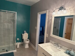 Ein Badezimmer mit Duschkabine aus Glas, Toilette, Waschbecken mit Marmorplatte und großem Spiegel.
