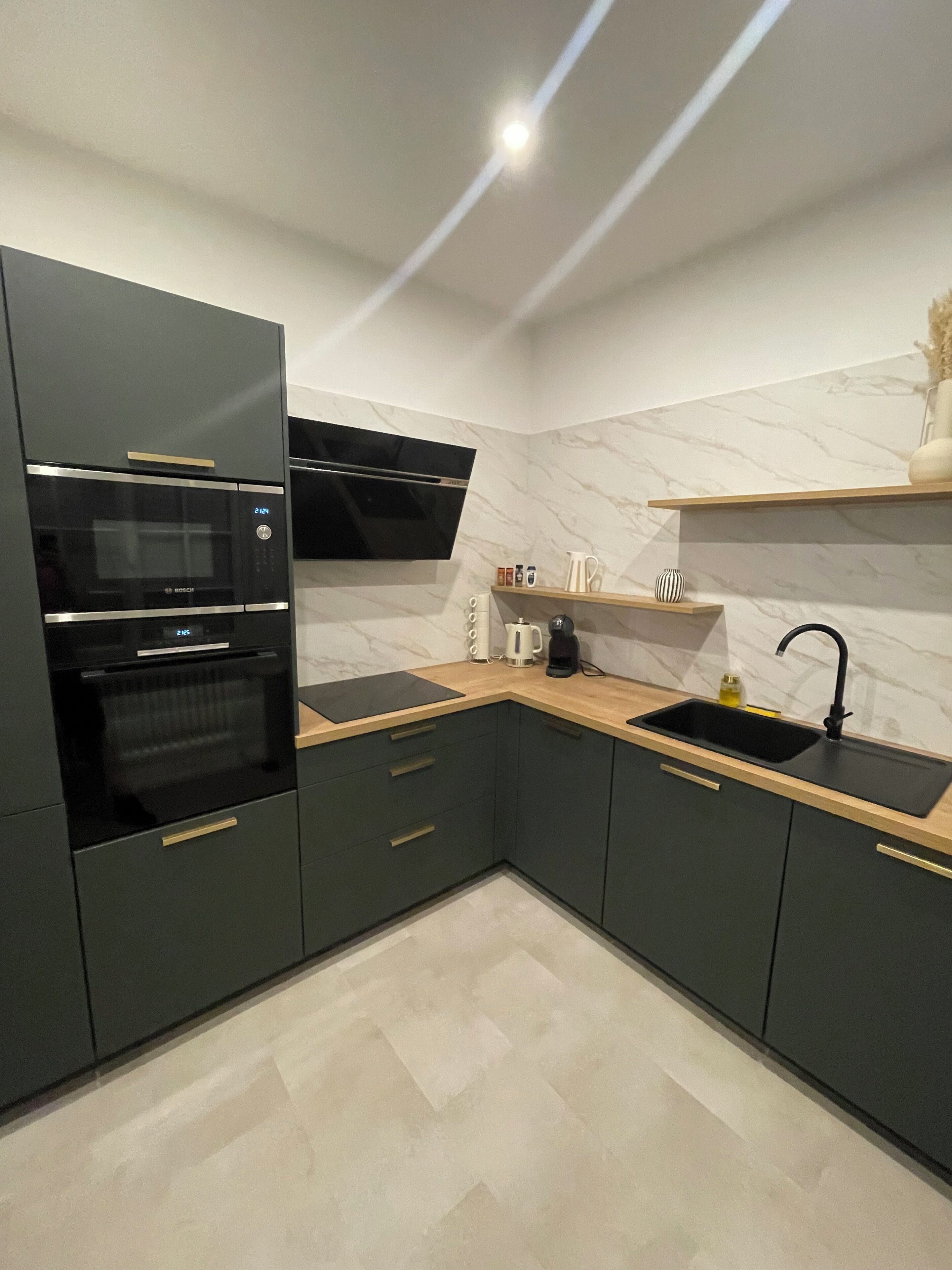 A modern kitchen with dark cabinetry, a built-in oven, a microwave, a sink, and a marble backsplash.