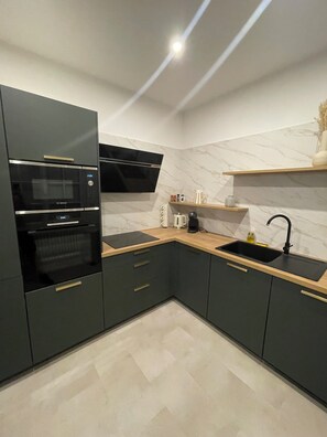 A modern kitchen with dark cabinetry, a built-in oven, a microwave, a sink, and a marble backsplash. - Elegance & Light in the Heart of Brest (3 bedrooms/6 guests) (Brest)