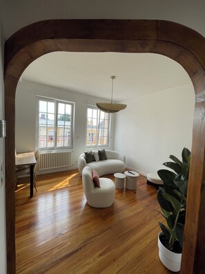 A modern living room with a wooden floor, a white sofa, a dining table, and a potted plant. - Elegance & Light in the Heart of Brest (3 bedrooms/6 guests) (Brest)
