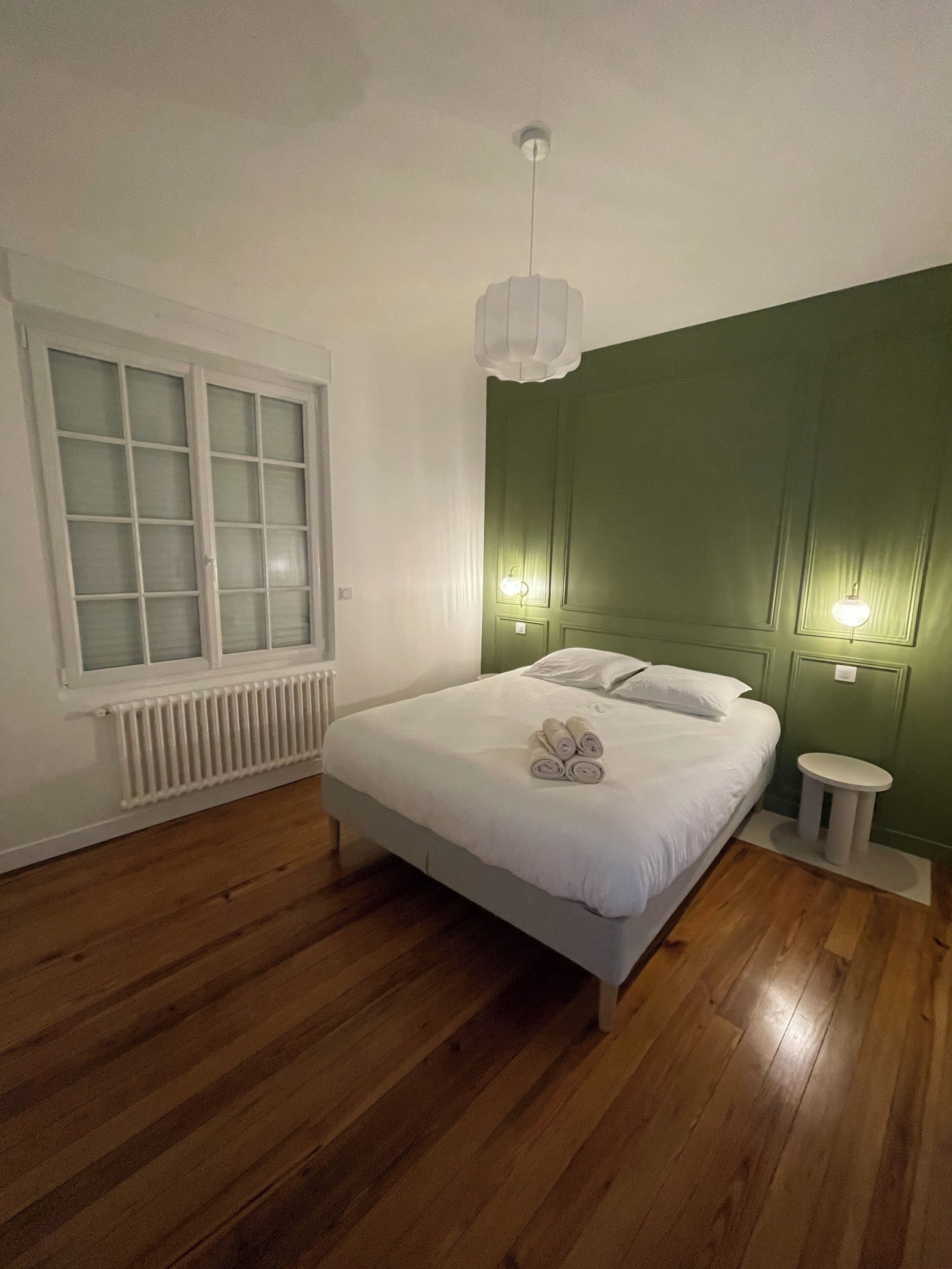 A bedroom with a bed, a radiator, a window with frosted glass, and a green accent wall.