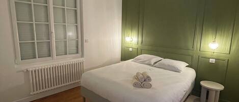 A bedroom with a bed, a radiator, a window with frosted glass, and a green accent wall.