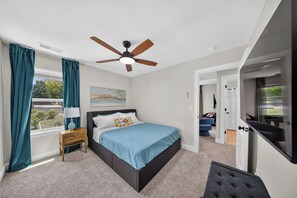 A bedroom with a bed, a nightstand, a ceiling fan, a window with curtains, and a door leading to another room. - Escape at this New Build with 3 Bedrooms King Bed at Kings Mountain Near Casino (Kings Mountain)