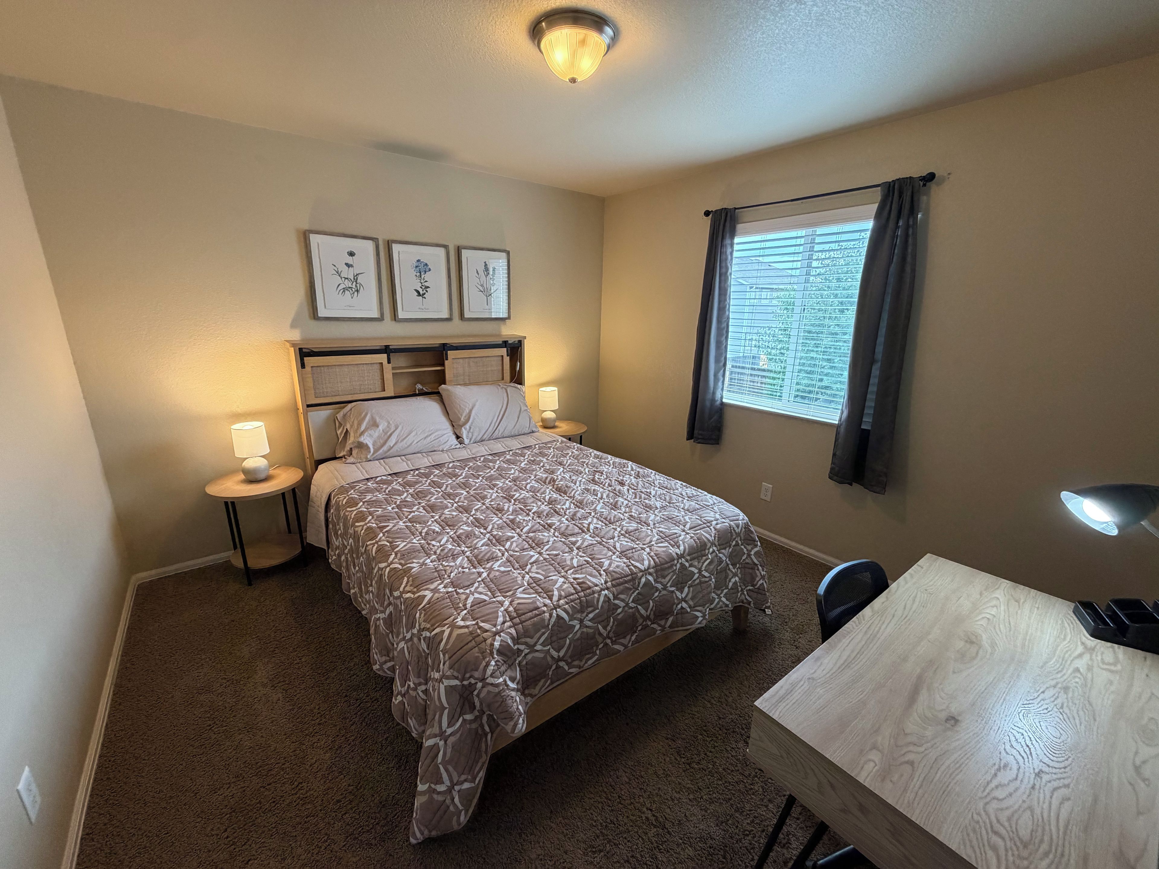 Une chambre à coucher avec un lit, des tables de chevet, un bureau et une fenêtre avec des rideaux.